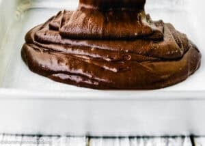 Thick chocolate brownie batter, inspired by The Best Eggless Chocolate Cake Ever, being poured into a parchment-lined baking pan.