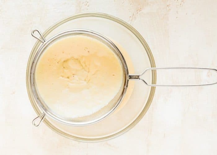 egg-free pastry cream being strained  through a fine-mesh sieve into a bowl.