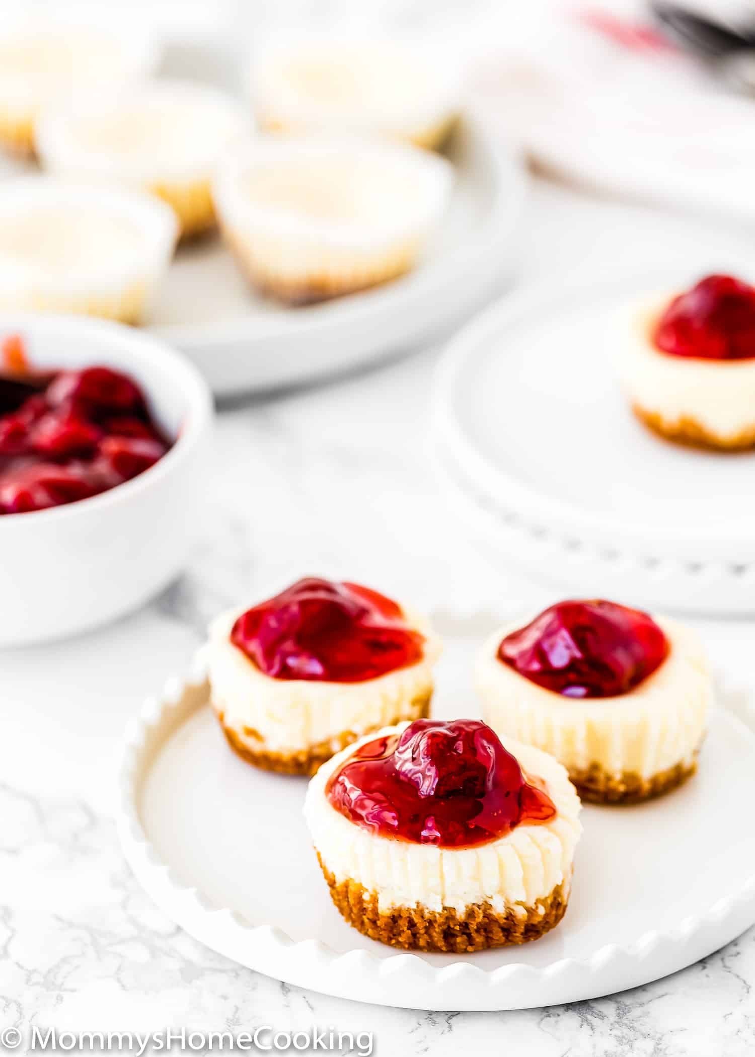 Three eggless mini cheesecakes on a plate with strawberry sauce on top.
