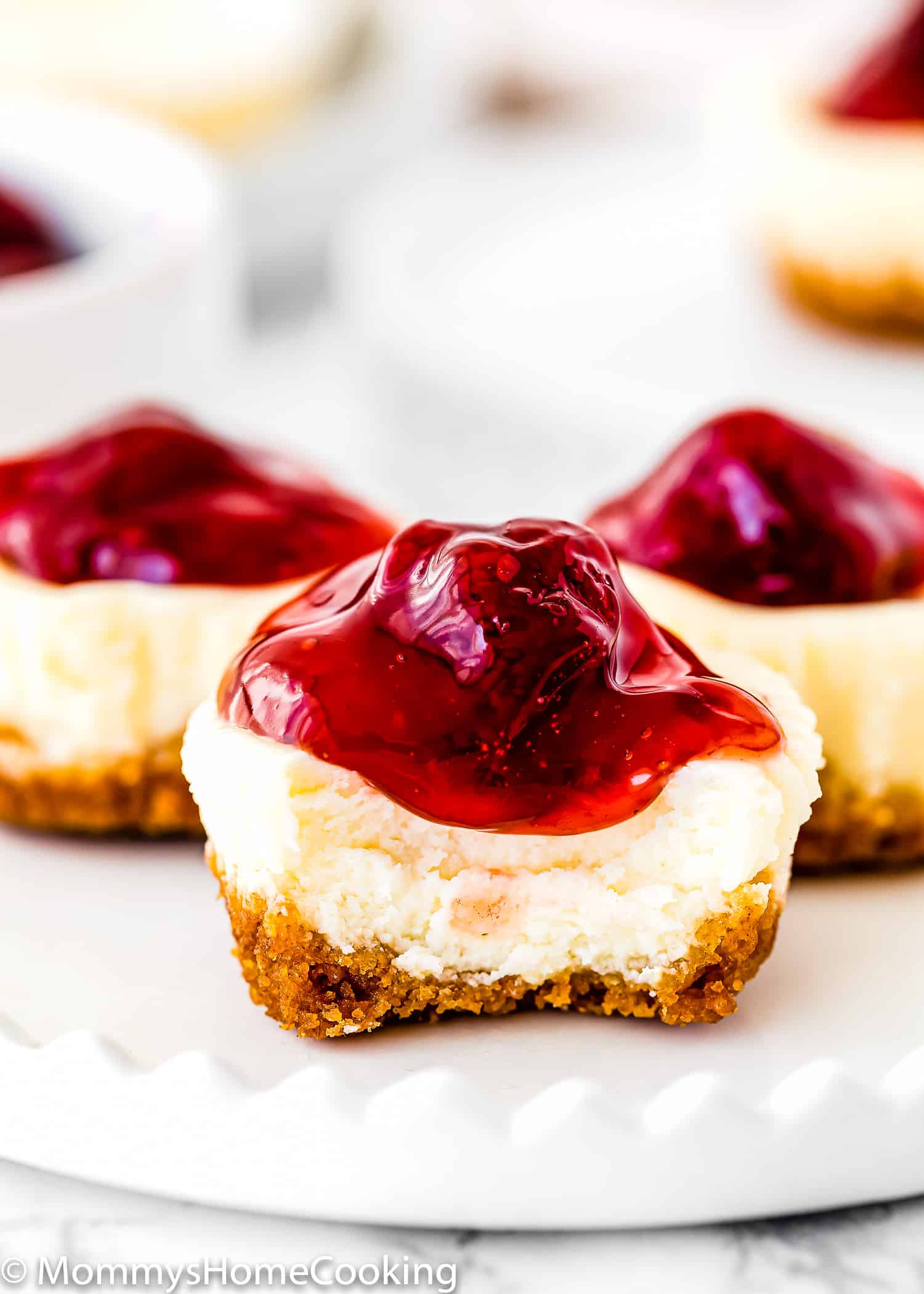 A bitten egg-free strawberry mini cheesecake on a plate showing its creamy texture.