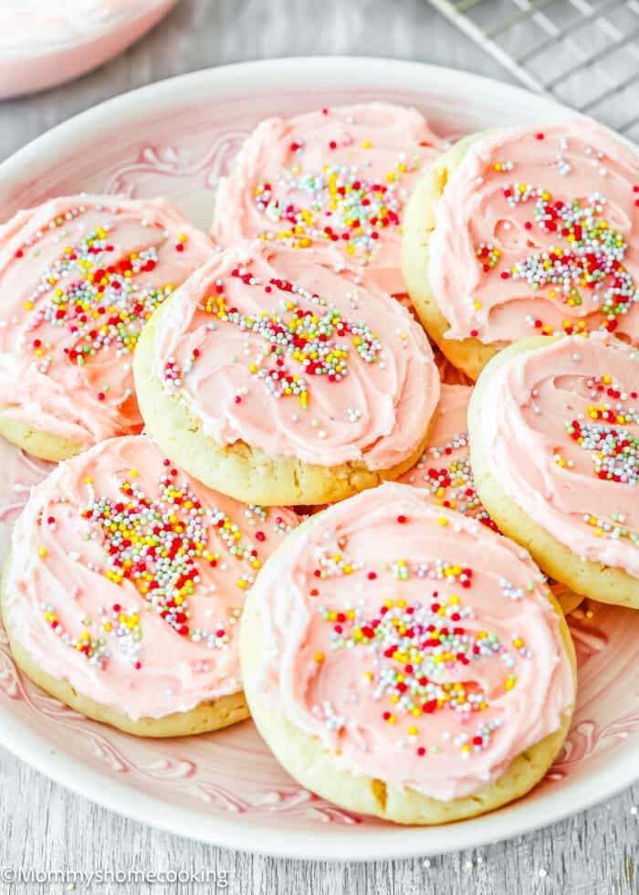 A plate with eggless sugar cookies frosted with pink buttercream and sprinkle.