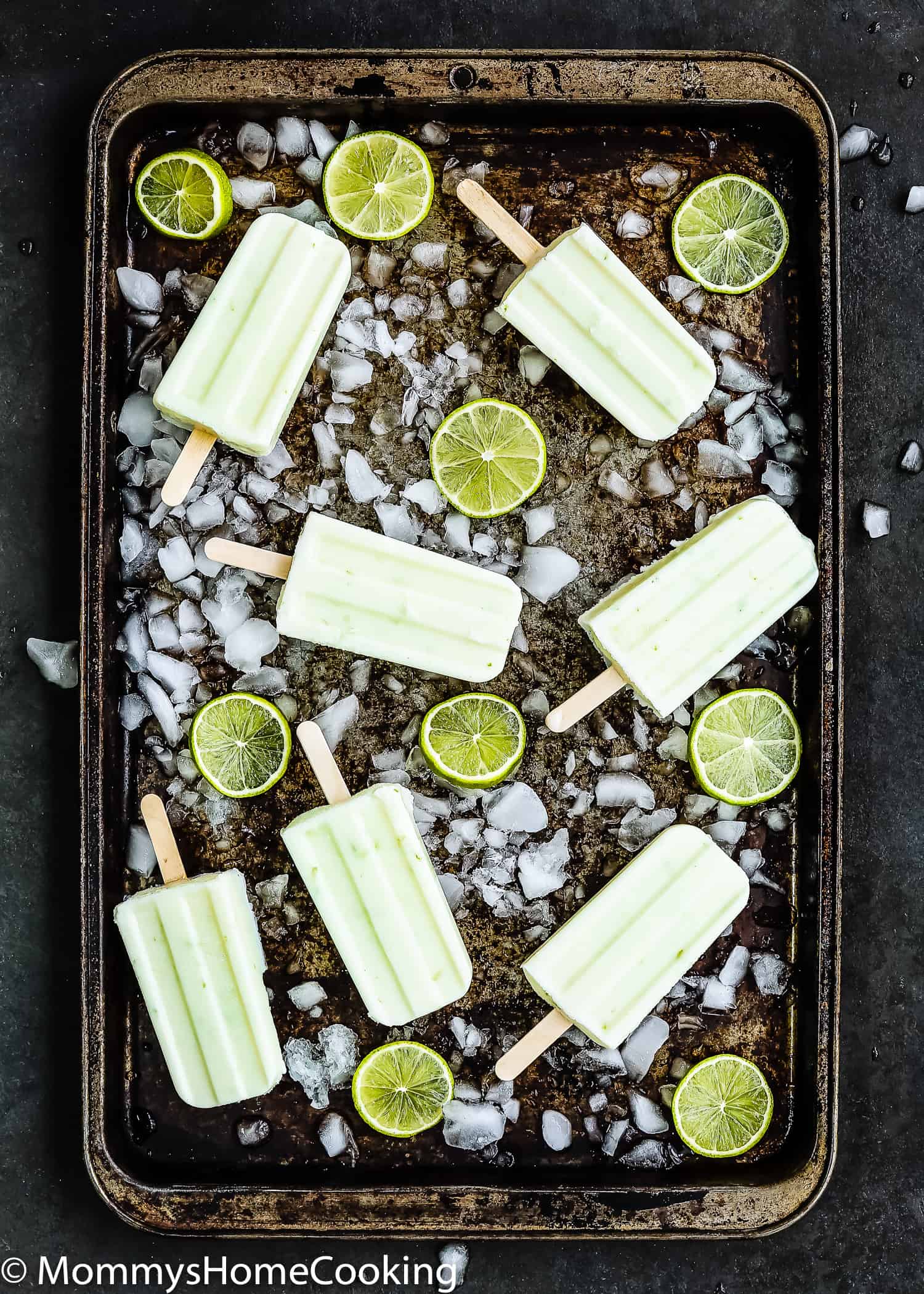 Healthy Key Lime Popsicles in a baking tray with chopped ice and lime slices.