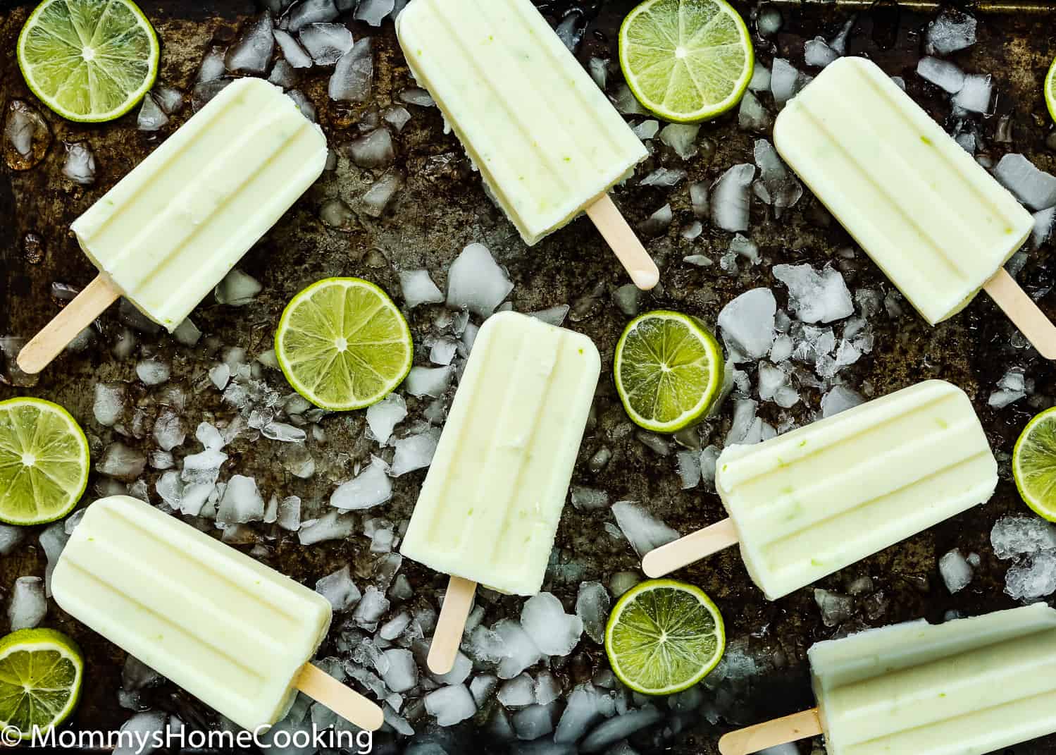 Easy and Healthy Key Lime Popsicles in a baking tray with chopped ice and lime slices.