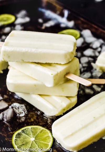 stack of four Easy and Healthy Key Lime Popsicles in a baking tray with chopped ice and lime slices.