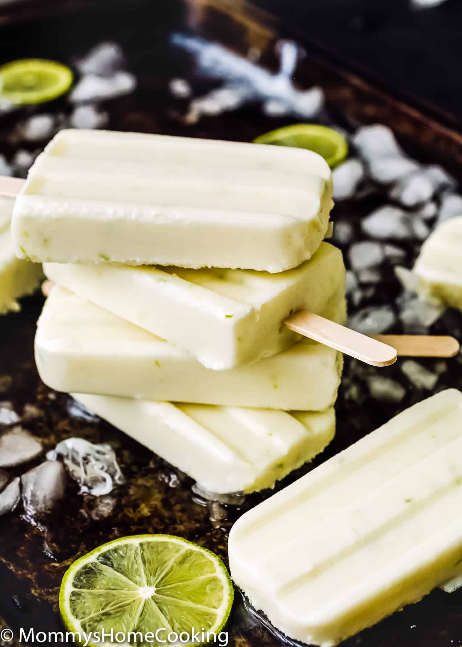stack of four Easy and Healthy Key Lime Popsicles in a baking tray with chopped ice and lime slices.