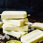 stack of Key Lime Popsicles in a baking tray with chopped ice and lime slices.