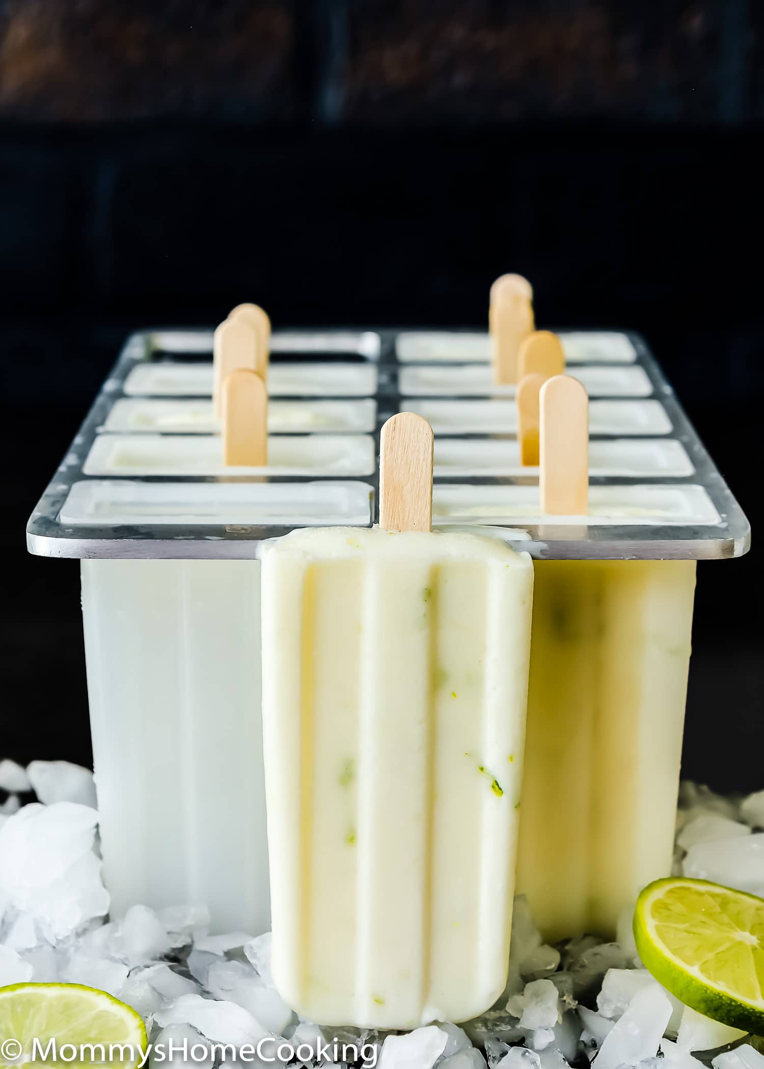 an Healthy Key Lime Popsicle next to a Popsicle mold with chopped ice and lime slices.