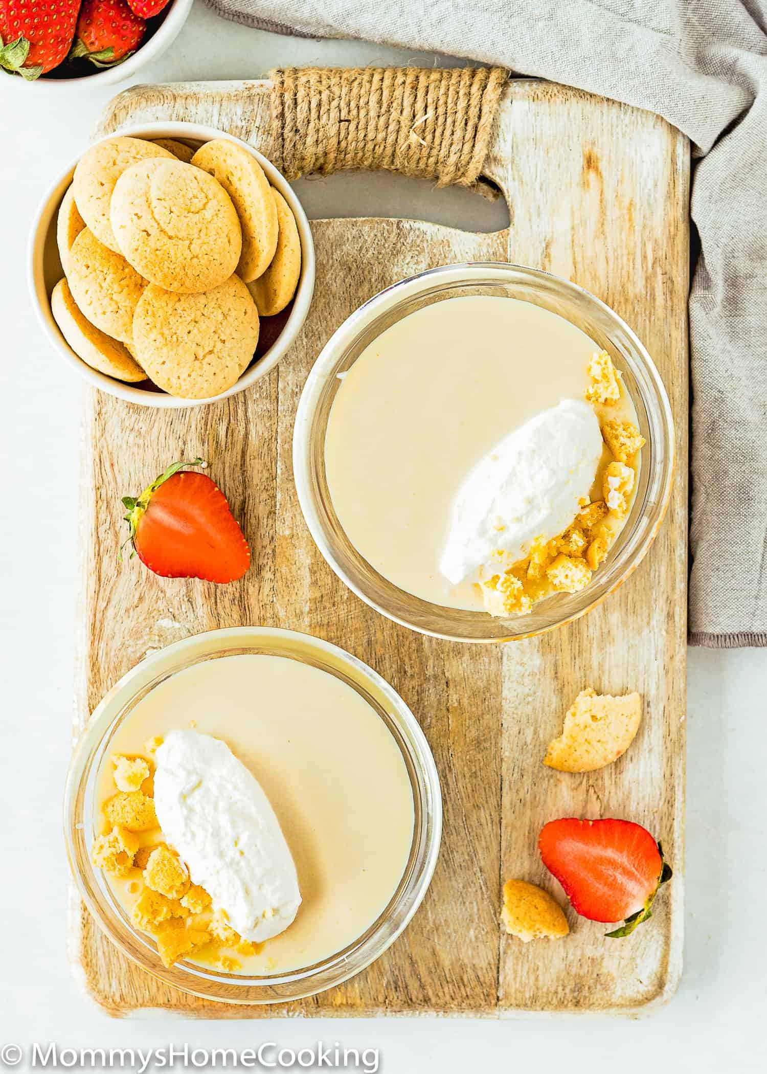two bowls with Egg free homemade vanilla pudding with whipped cream over a wooden board with fresh strawberries and more vanilla wafers.