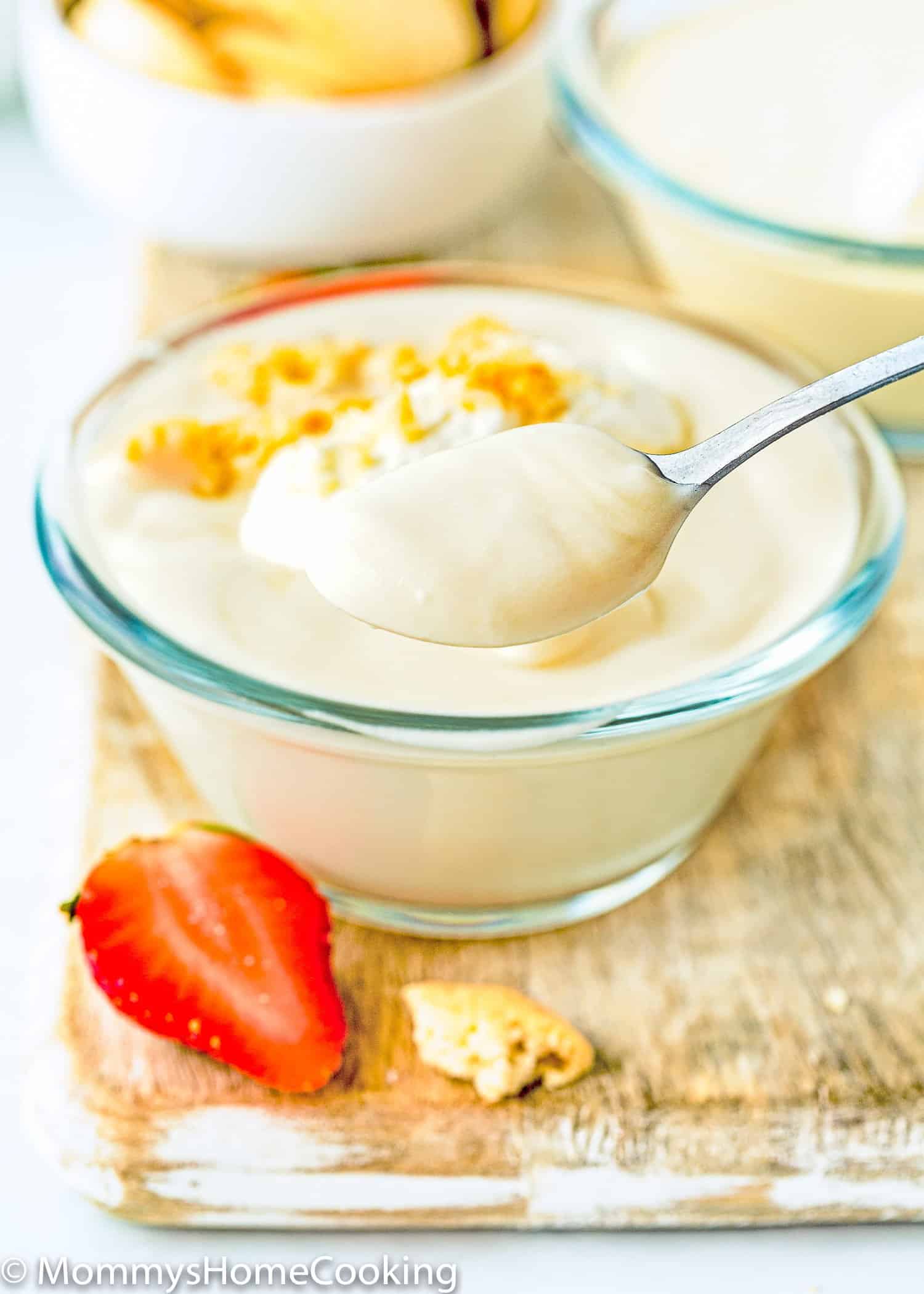 a spoon with Egg free homemade vanilla pudding and two bowls in the background.