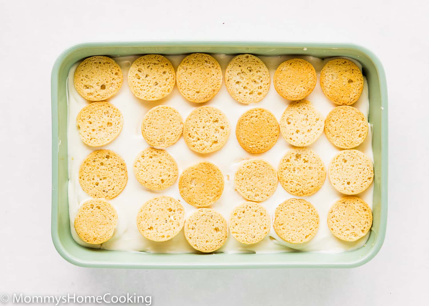 A layer of banana pudding in a rectangular green dish with homemade egg-free vanilla wafers on top.