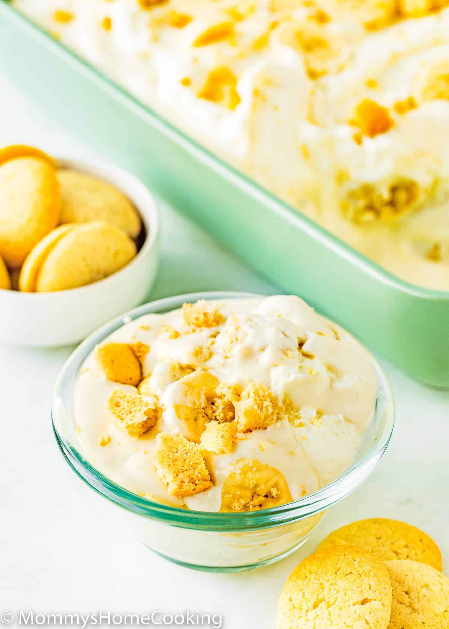 Eggless banana pudding in a small bowl with wafers and a big rectangular dish in the background.