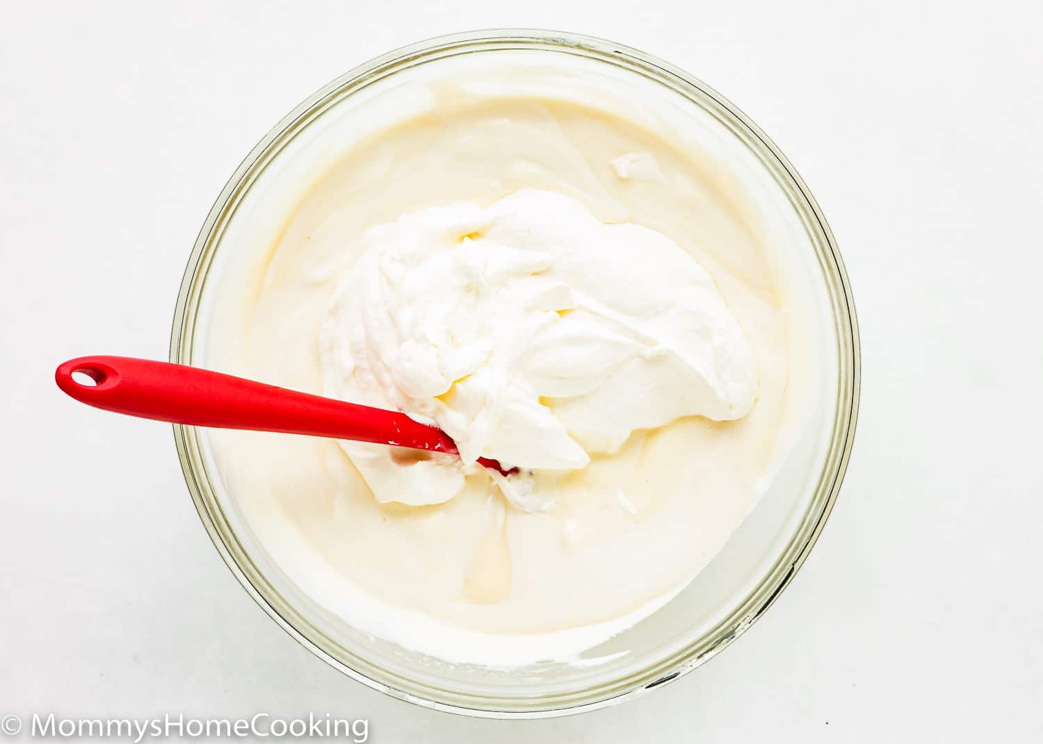 Eggless vanilla pudding with whipped cream and a red spatula.
