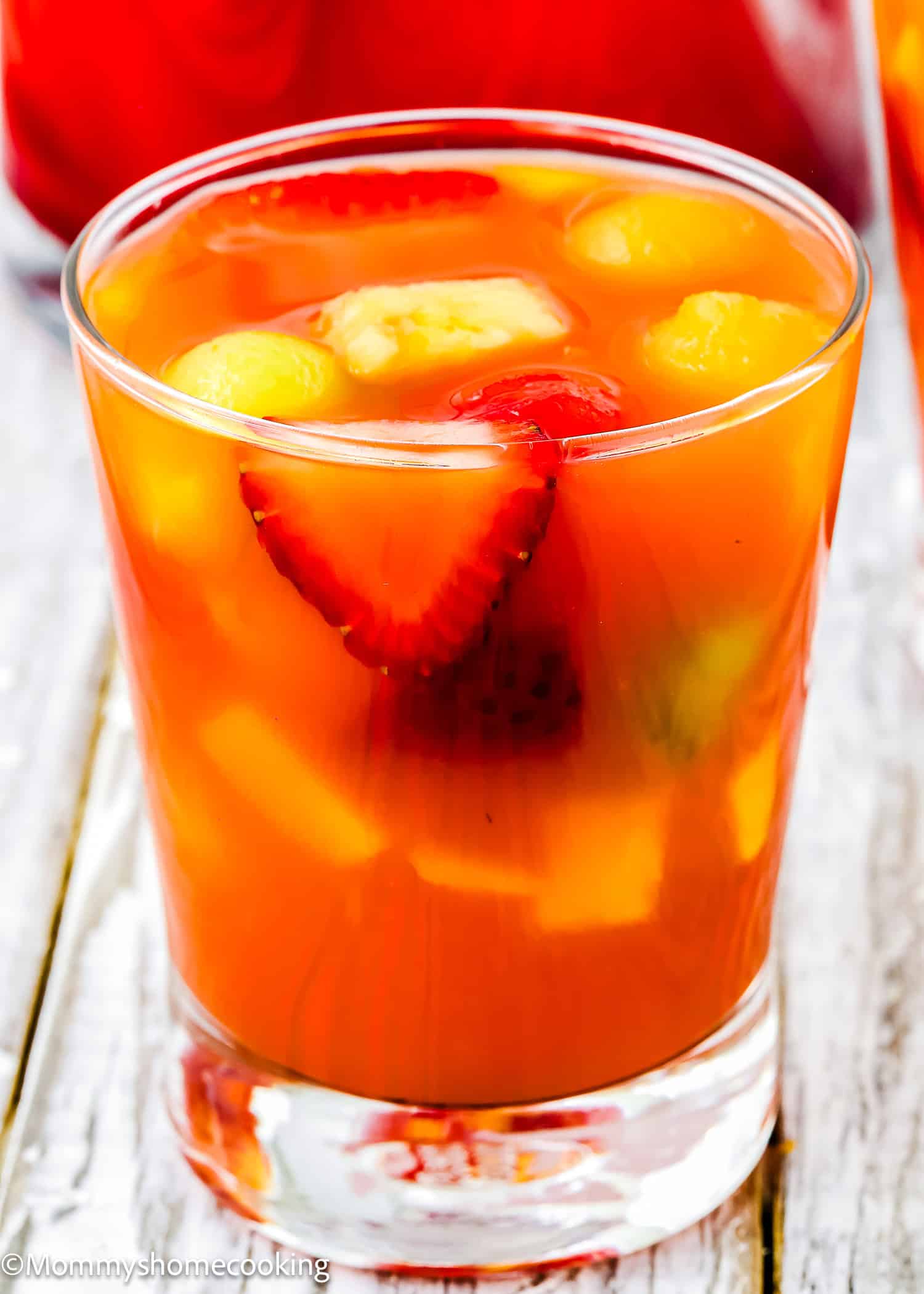 A glass of Venezuelan Tizana (Easy Fruit Punch Mocktail) with sliced strawberries and melon balls, served on a light wooden surface.
