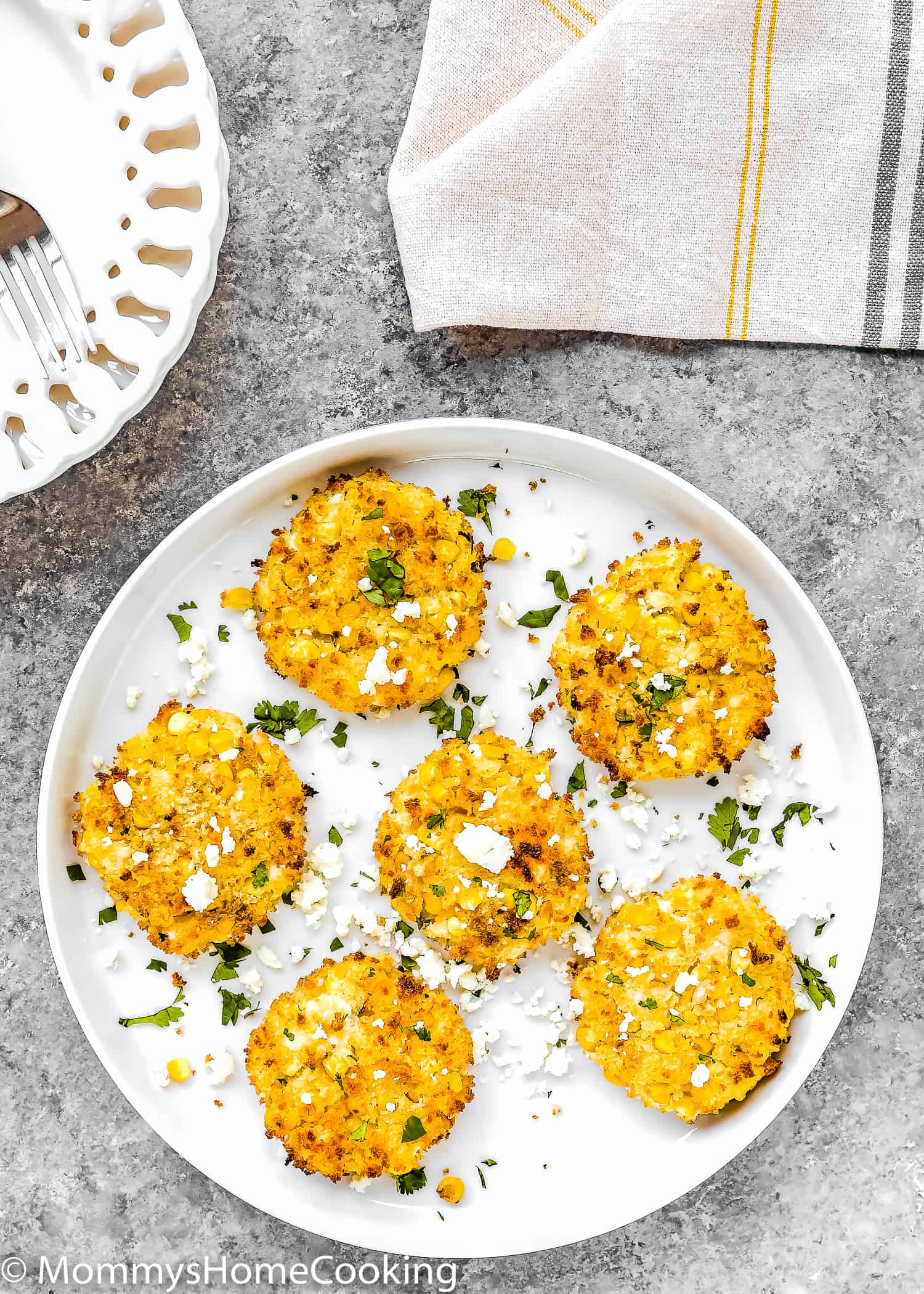 eggless corn fritters on a plate over a grey surface with two white plate on the side and a kitchen towel.