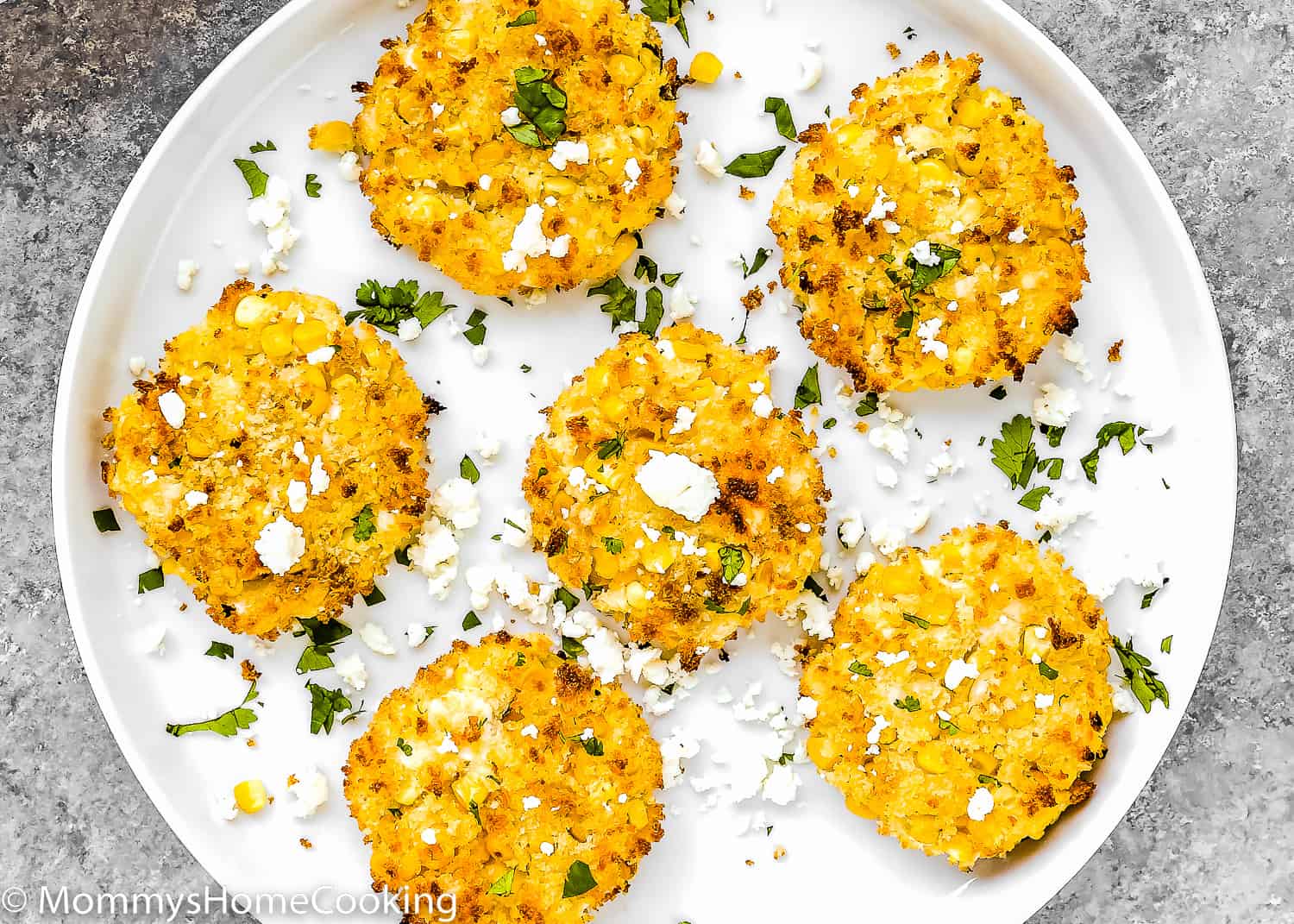 six egg-free corn fritter in a plate with cheese and chopped cilantro.
