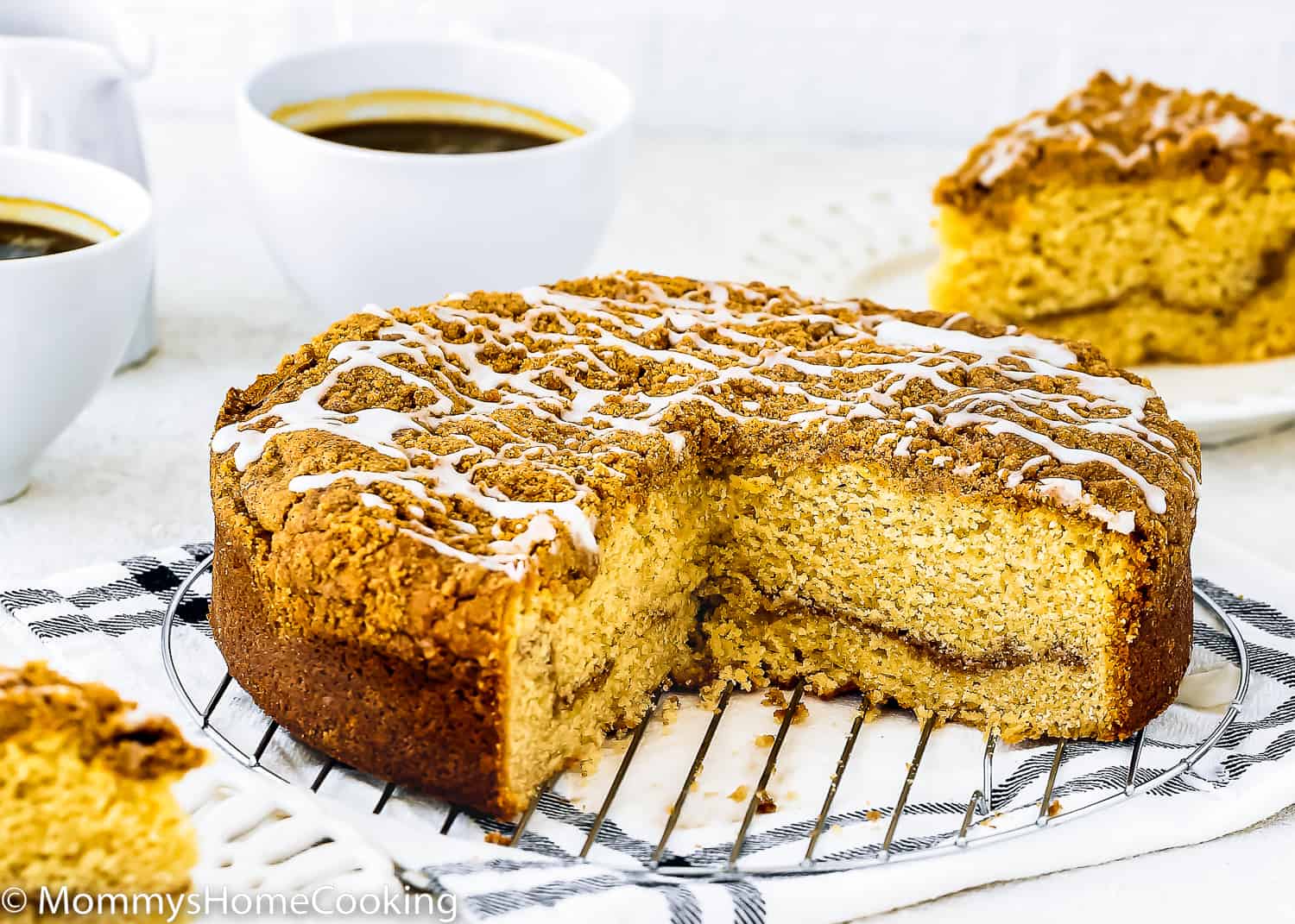 A sliced Eggless Coffee Cake with streusel on top over a cooling rack with two cup of coffee on the background.