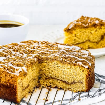 A sliced Eggless Coffee Cake over a cooling rack with a slice on the background.