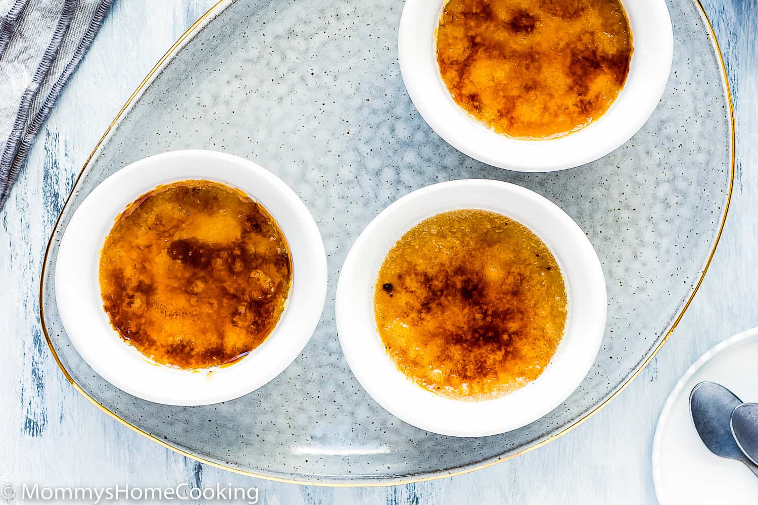 three egg-free creme brulee with a sugar caramelized top over a blue serving plate.