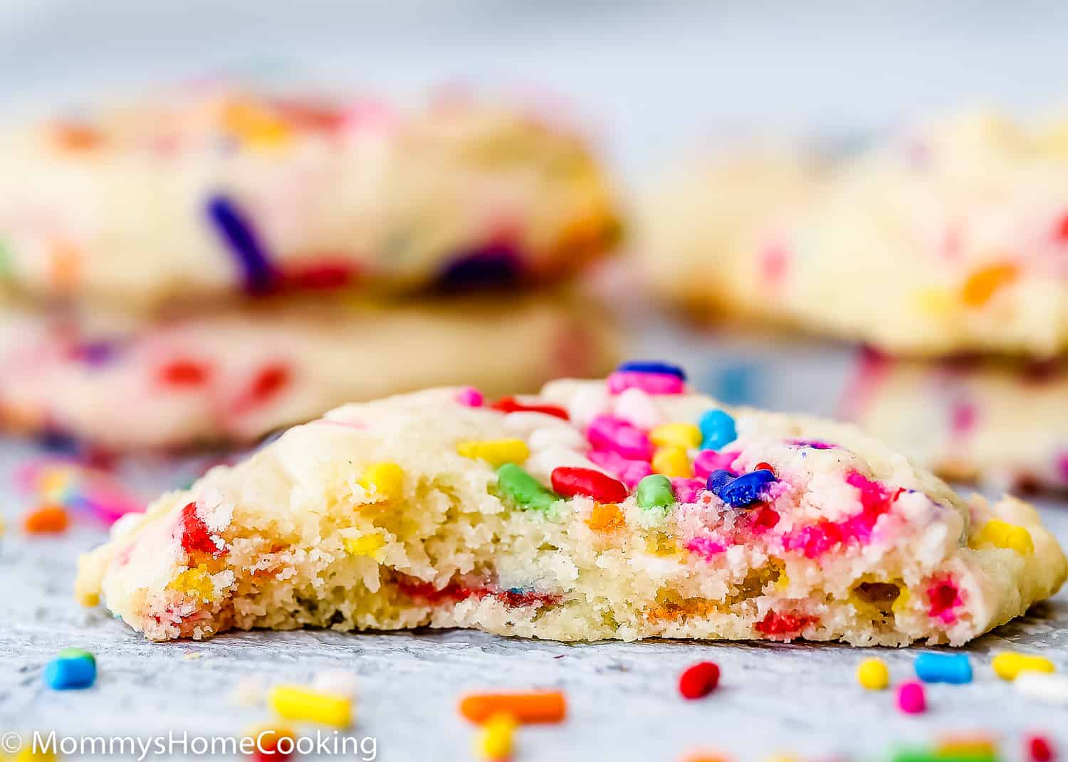 a egg-free Funfetti cookie bitten over a blue surface with sprinkles around it.