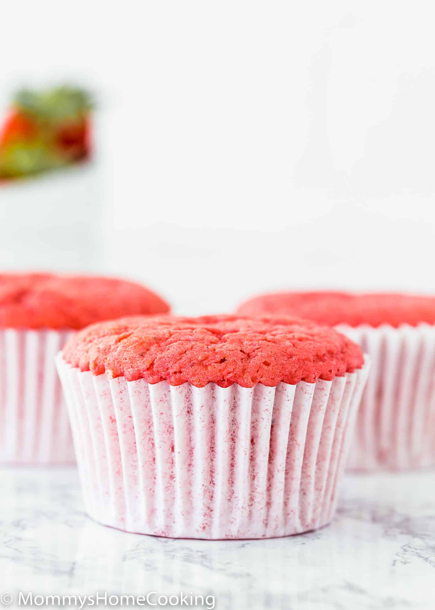 three Strawberry cupcakes without eggs over a marble surface.