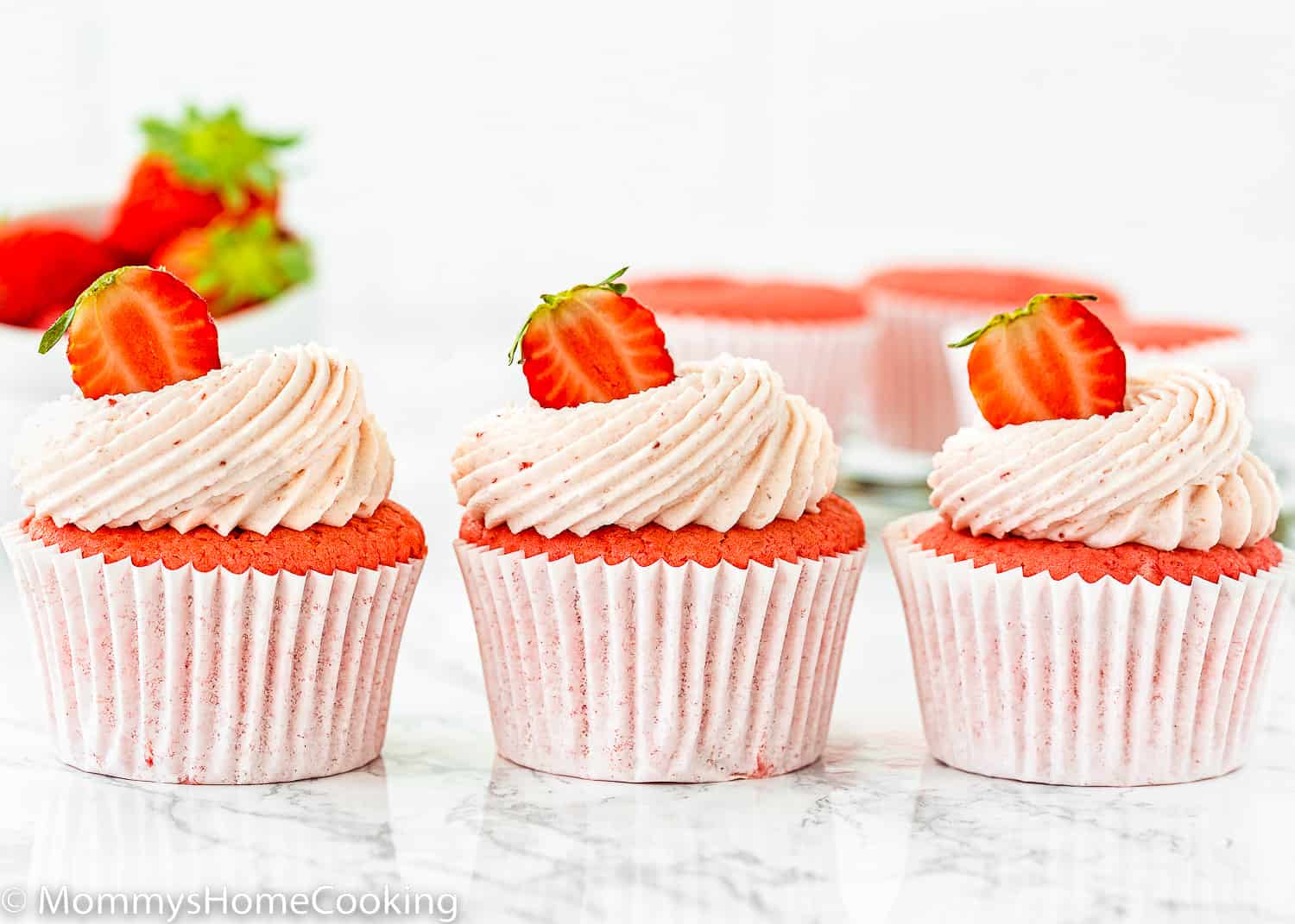 three egg-free Strawberry cupcakes lined up with strawberry buttercream and fresh Strawberry on top.
