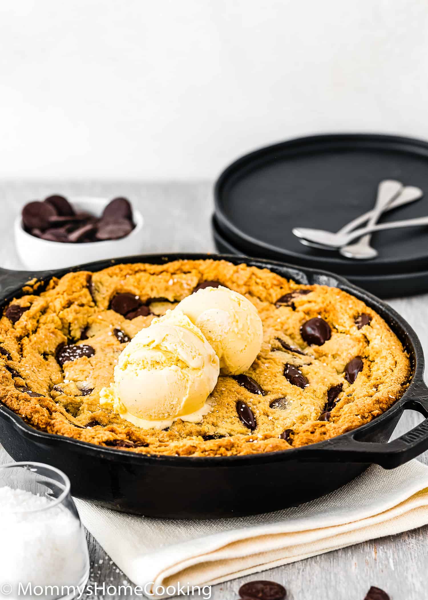 Eggless Chocolate Chip Skillet Cookie with two black plates and dessert spoons in the background.