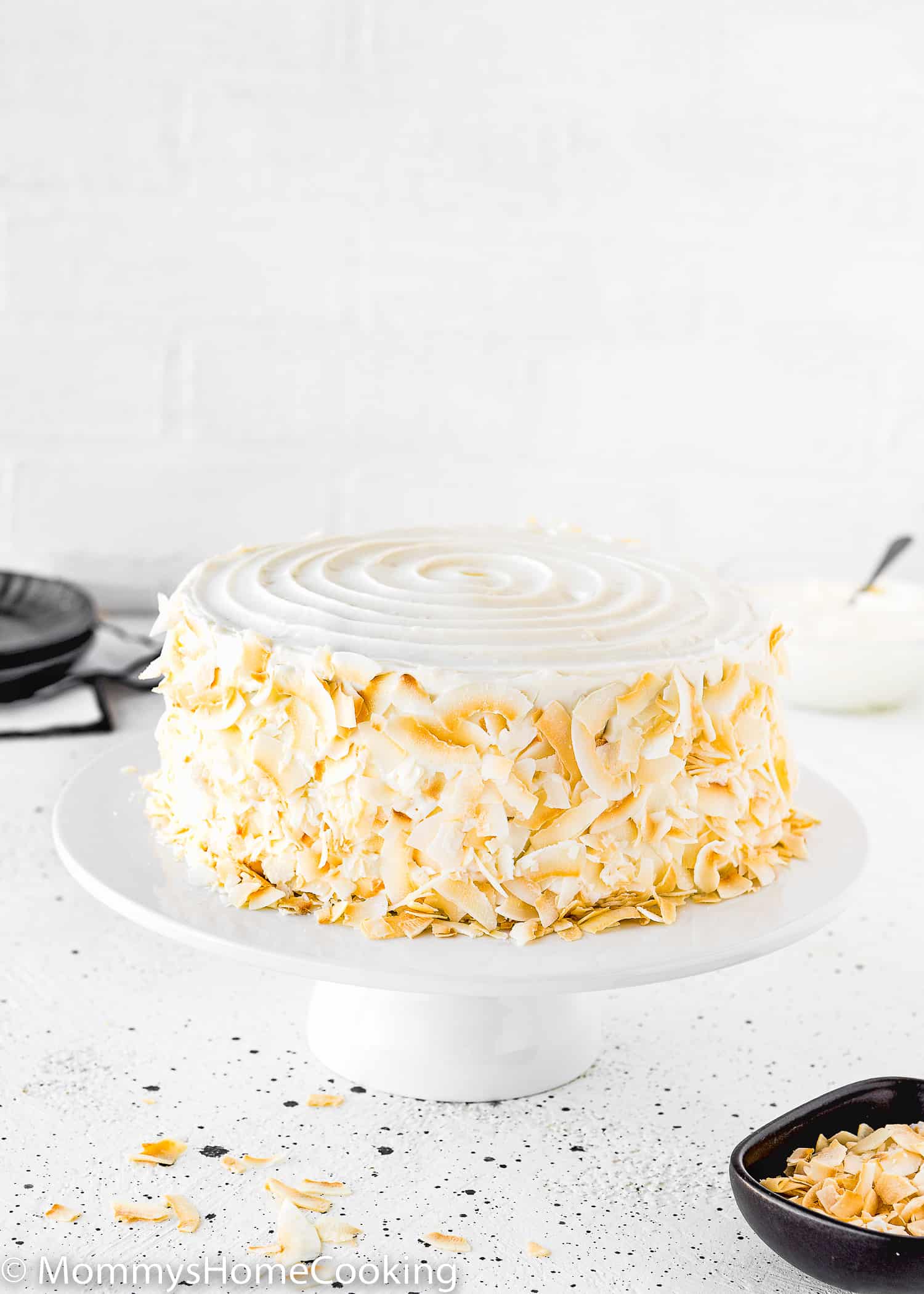 An Eggless Coconut Cake decorated with toasted coconut on a cake stand.
