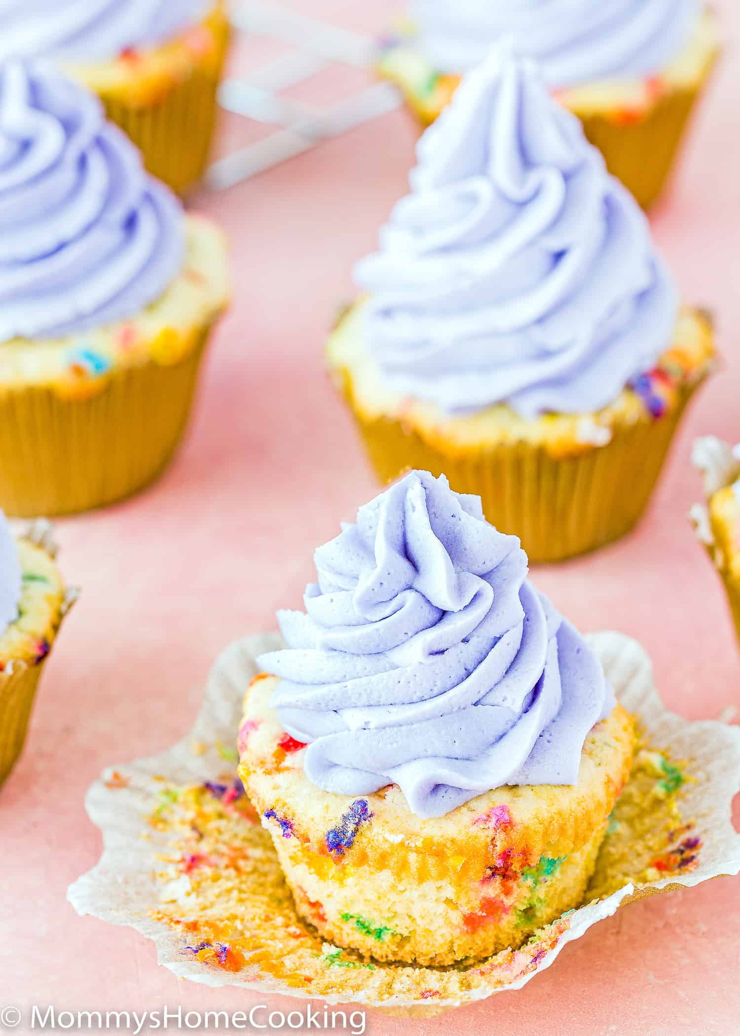Eggless Funfetti Cupcakes with purple buttercream over a pink surface.