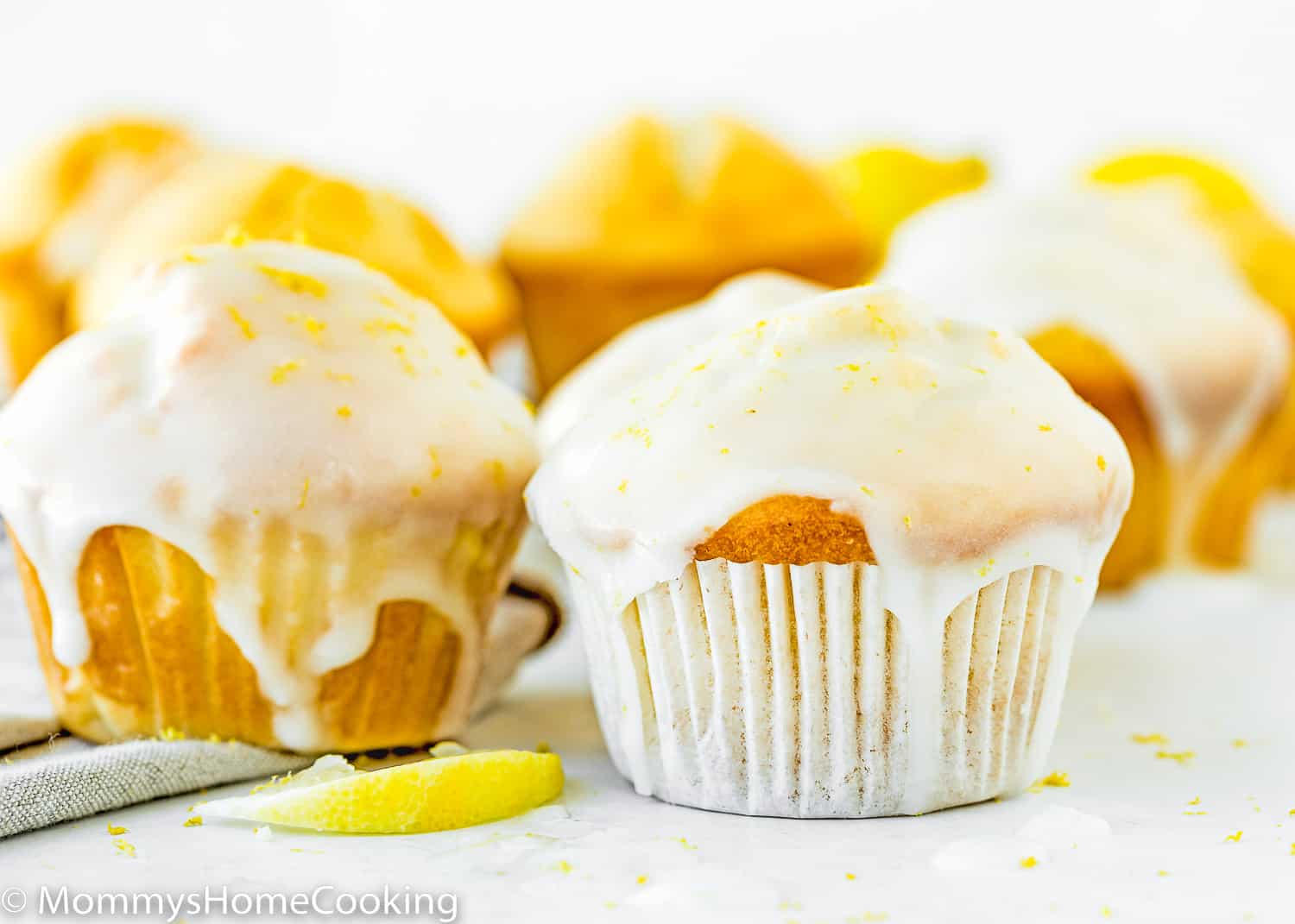 Eggless Lemon Muffins over a white surface with a lemon slice on the side.