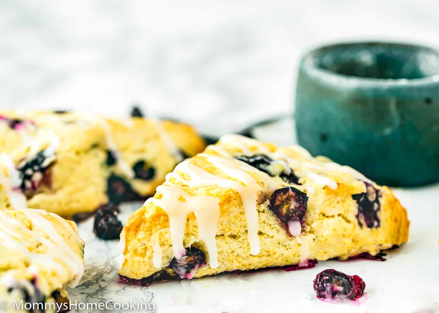 Eggless Blueberry Scones drizzled with glaze over a marble surface.