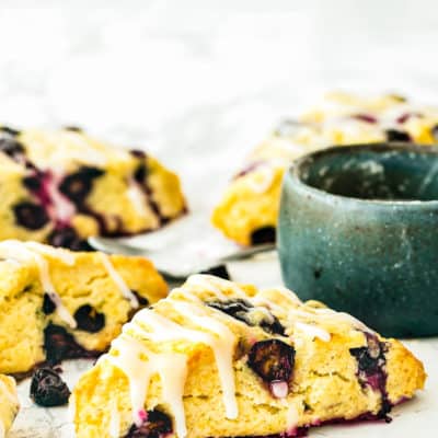 Eggless Blueberry Scones drizzled with lemon glaze over a marble surface.