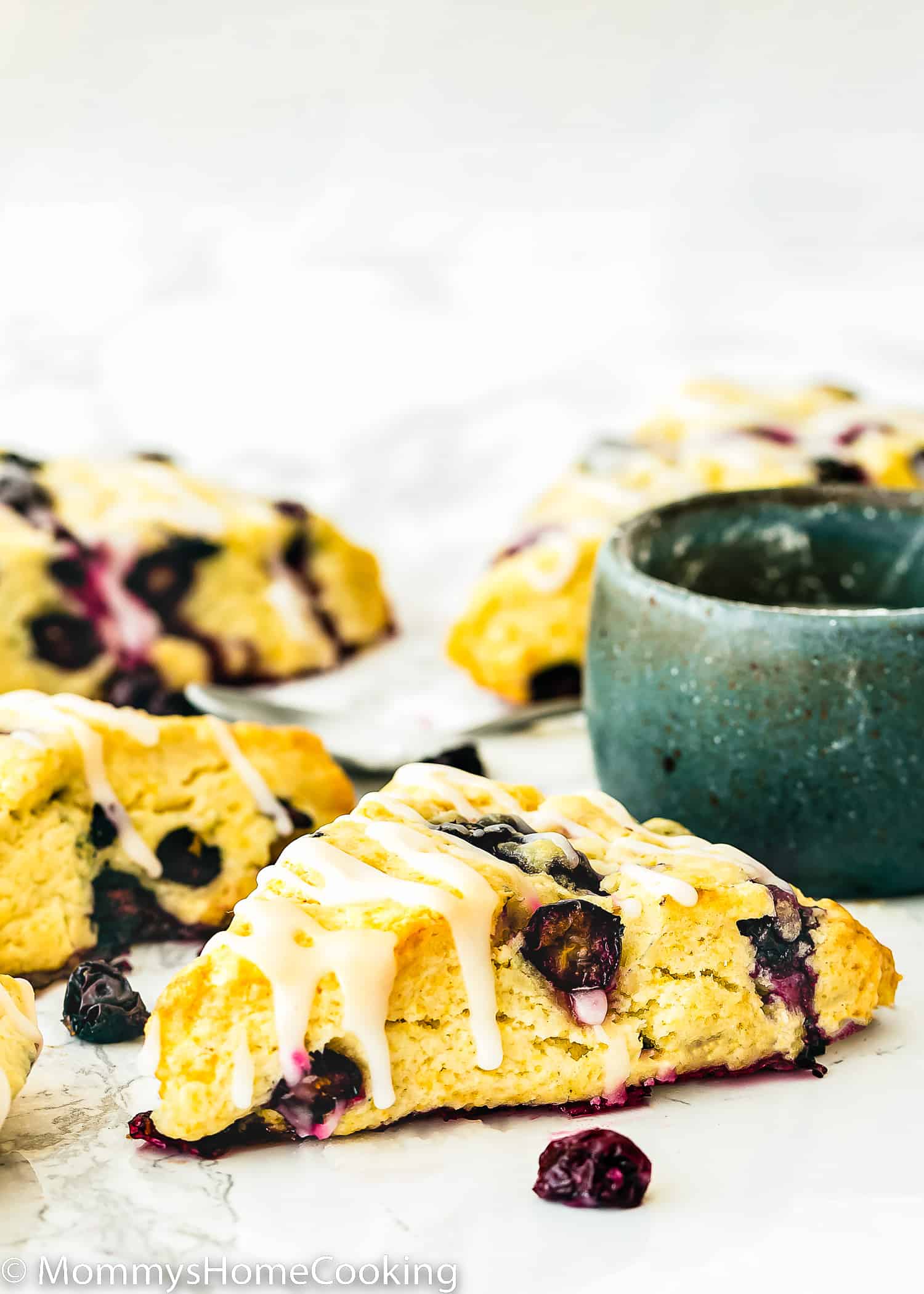 Eggless Blueberry Scones drizzled with lemon glaze over a marble surface.