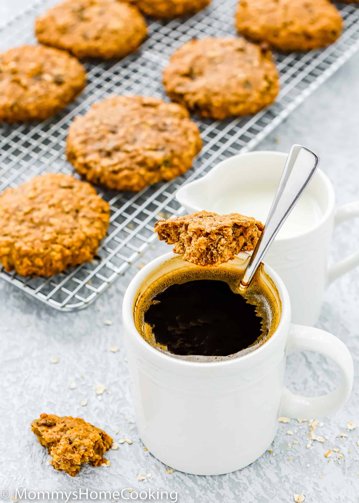 a cup of coffee with a spoon and a piece of Dairy-Free & Egg-Free Healthy Breakfast Cookie with more cookies over a cooling rack in the background.