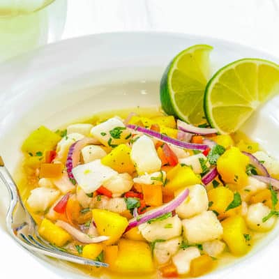 fish ceviche with mango in a white plate with a fork and a glass of wine in the background.