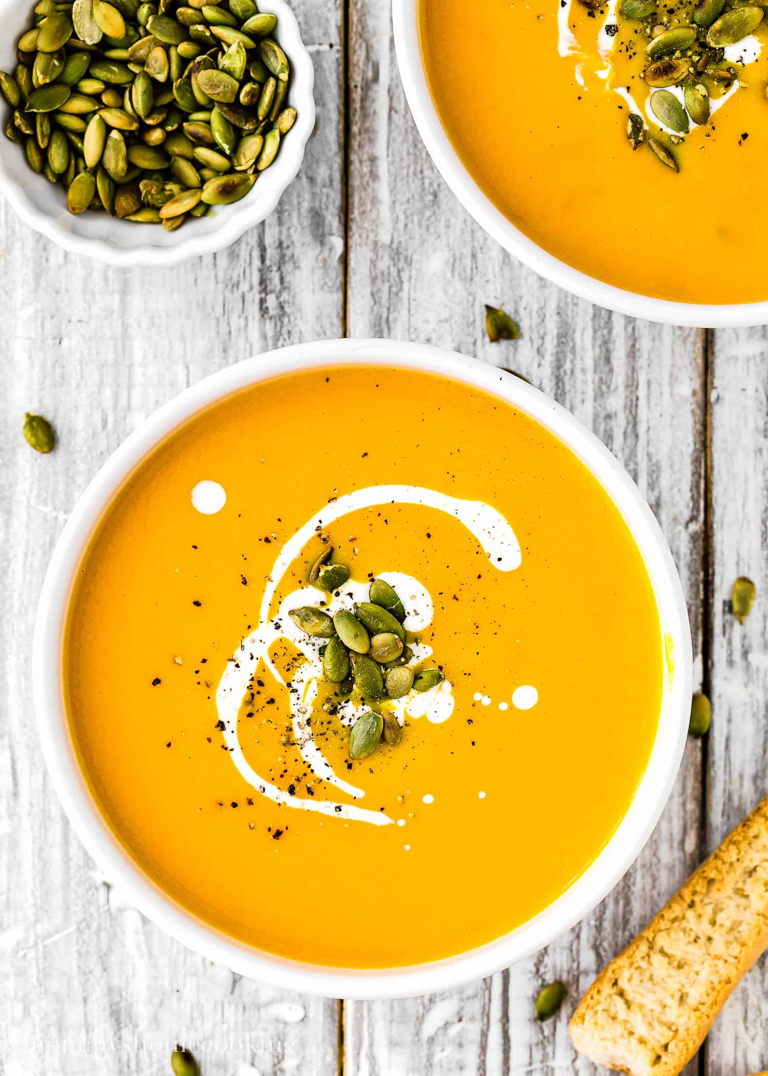 two bowls of Easy and Simple Pumpkin Soup garnished with cream and roasted pumpkin seeds.