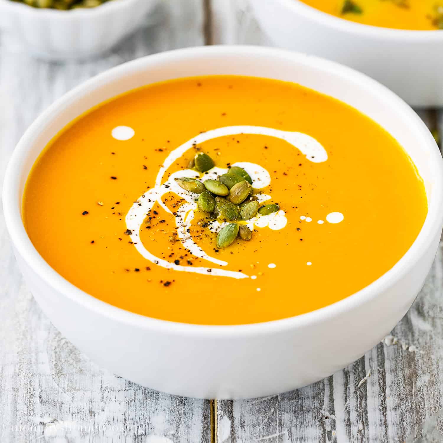 Easy and Simple Pumpkin Soup in a bowl garnished with cream and roasted pumpkin seeds.
