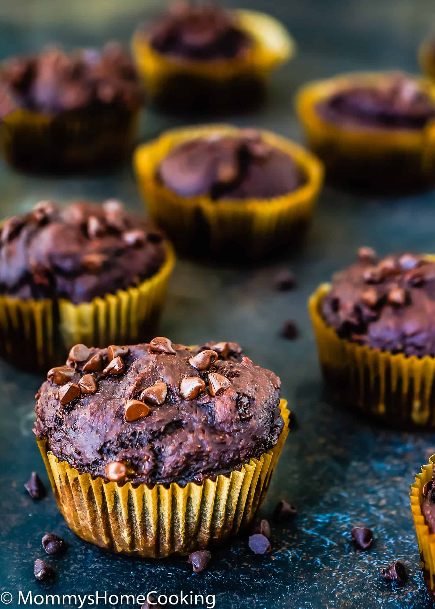 Eggless Banana Chocolate Muffins over a dark blue surface with chocolate chips around them.