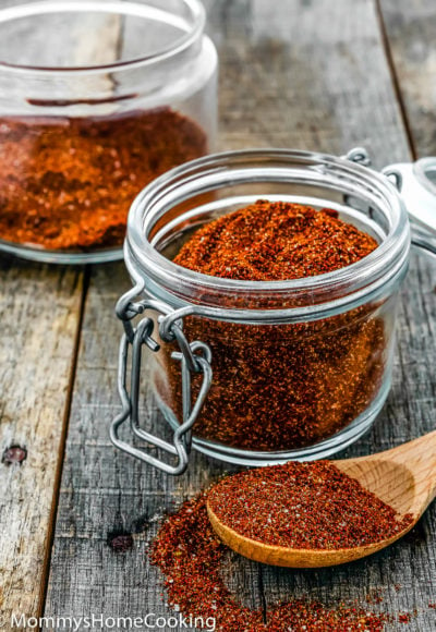 a glass jar filled with spicy taco seasoning over a wooden surface.