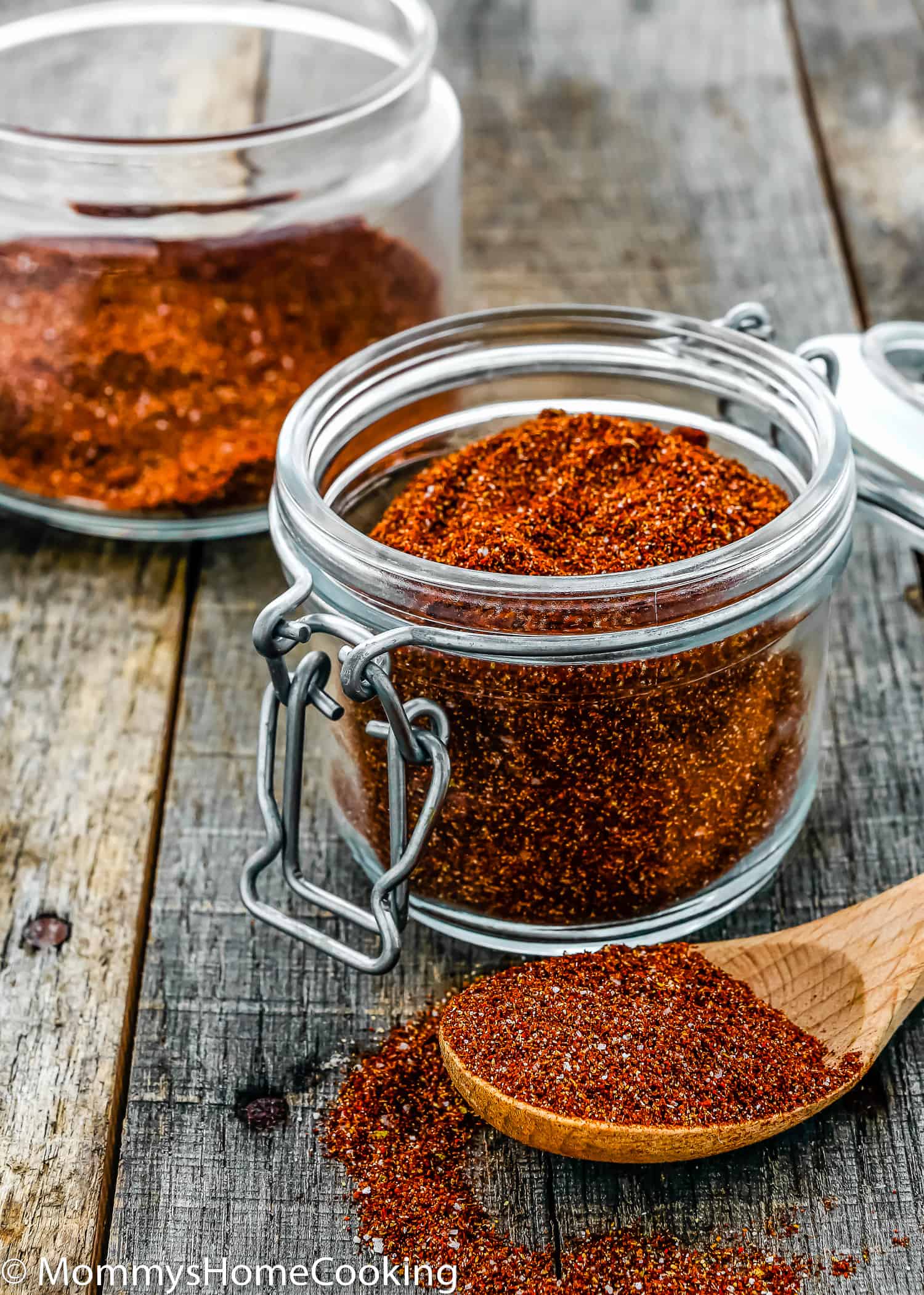 a glass jar filled with spicy taco seasoning over a wooden surface.