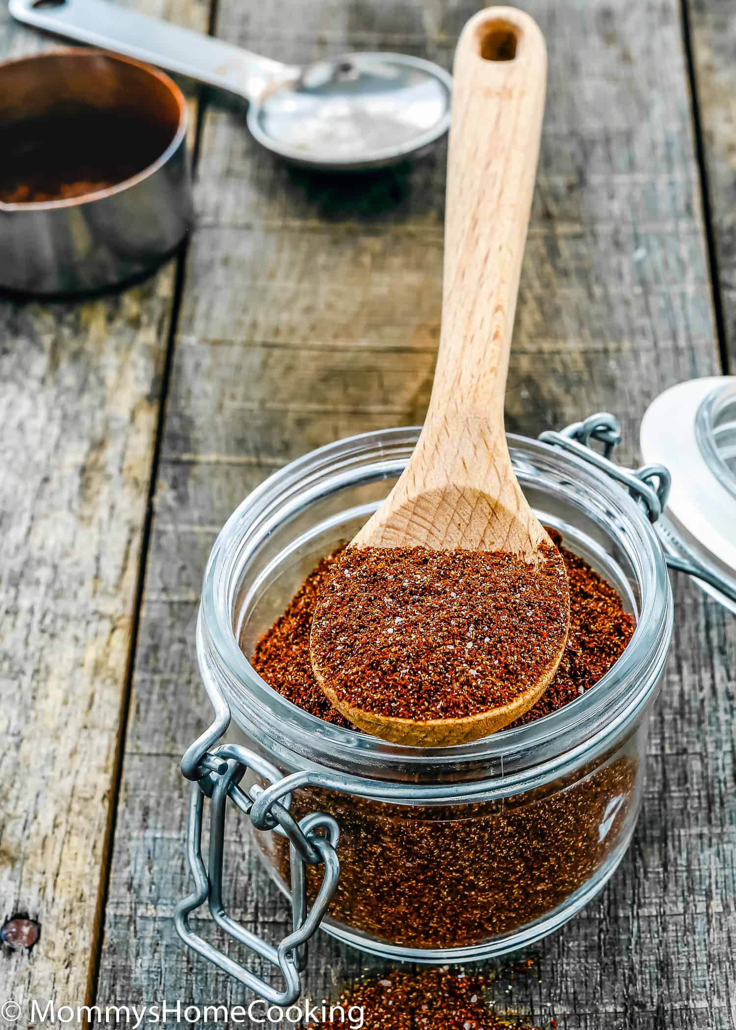 a wooden spoon with spicy taco seasoning over a glass jar.