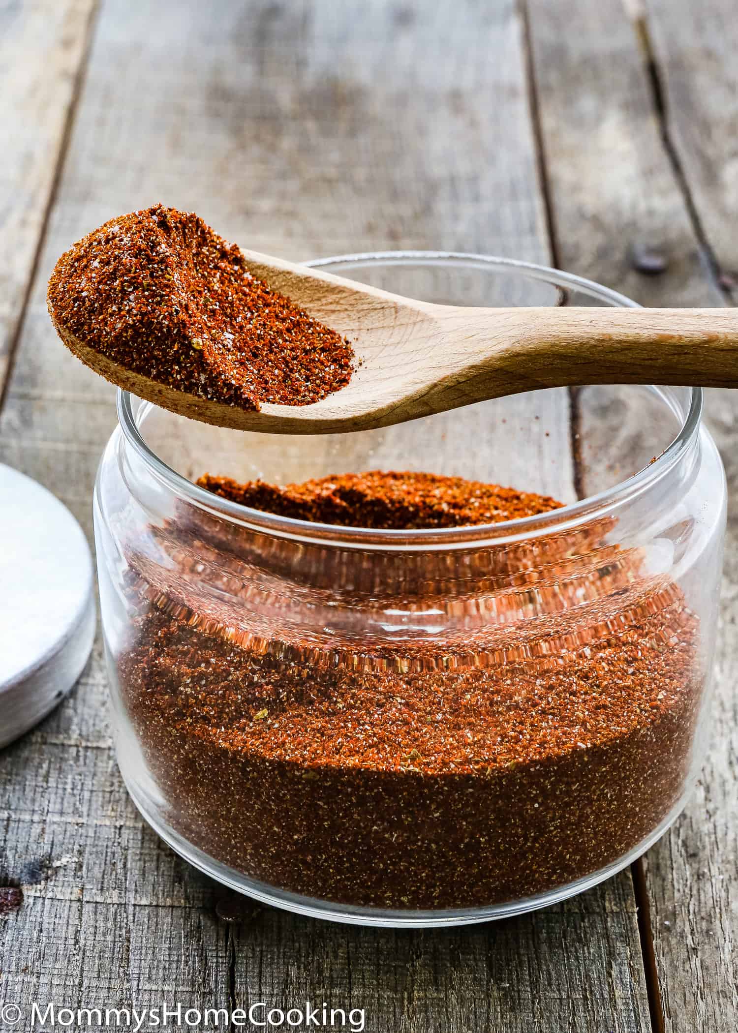 a wooden spoon with spicy taco seasoning over a glass jar over a wooden surface.