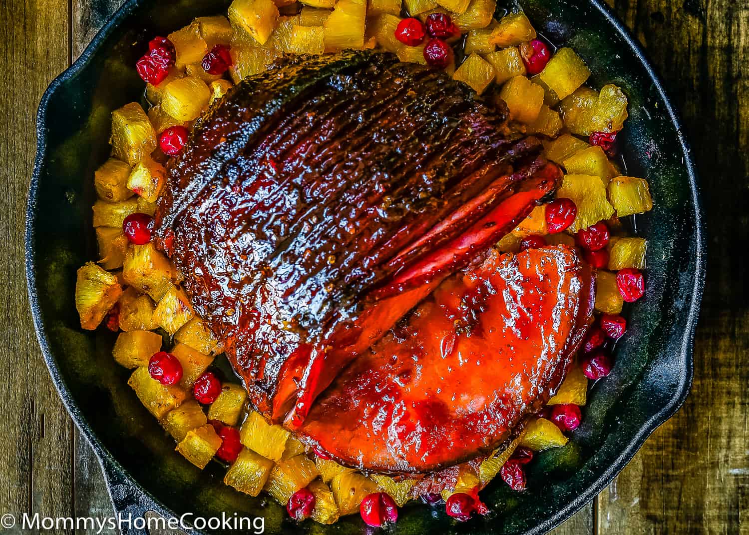a glazed ham in a cash iron skillet with pineapple and cranberries.