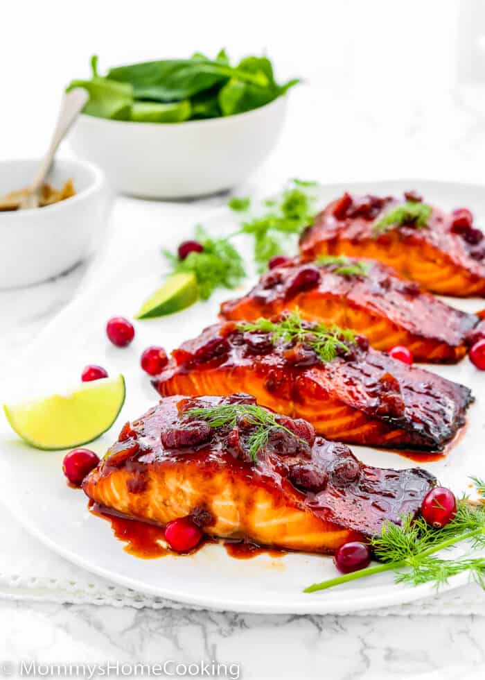 Cranberry Honey Glazed Salmon in a serving plate with fresh cranberries, lemon slices and dill over a marble surface.