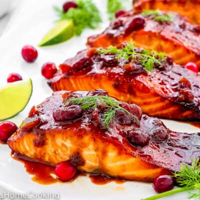 baked Cranberry Honey Glazed Salmon in a serving plate with fresh cranberries, lemon slices, dill and fresh cranberries.