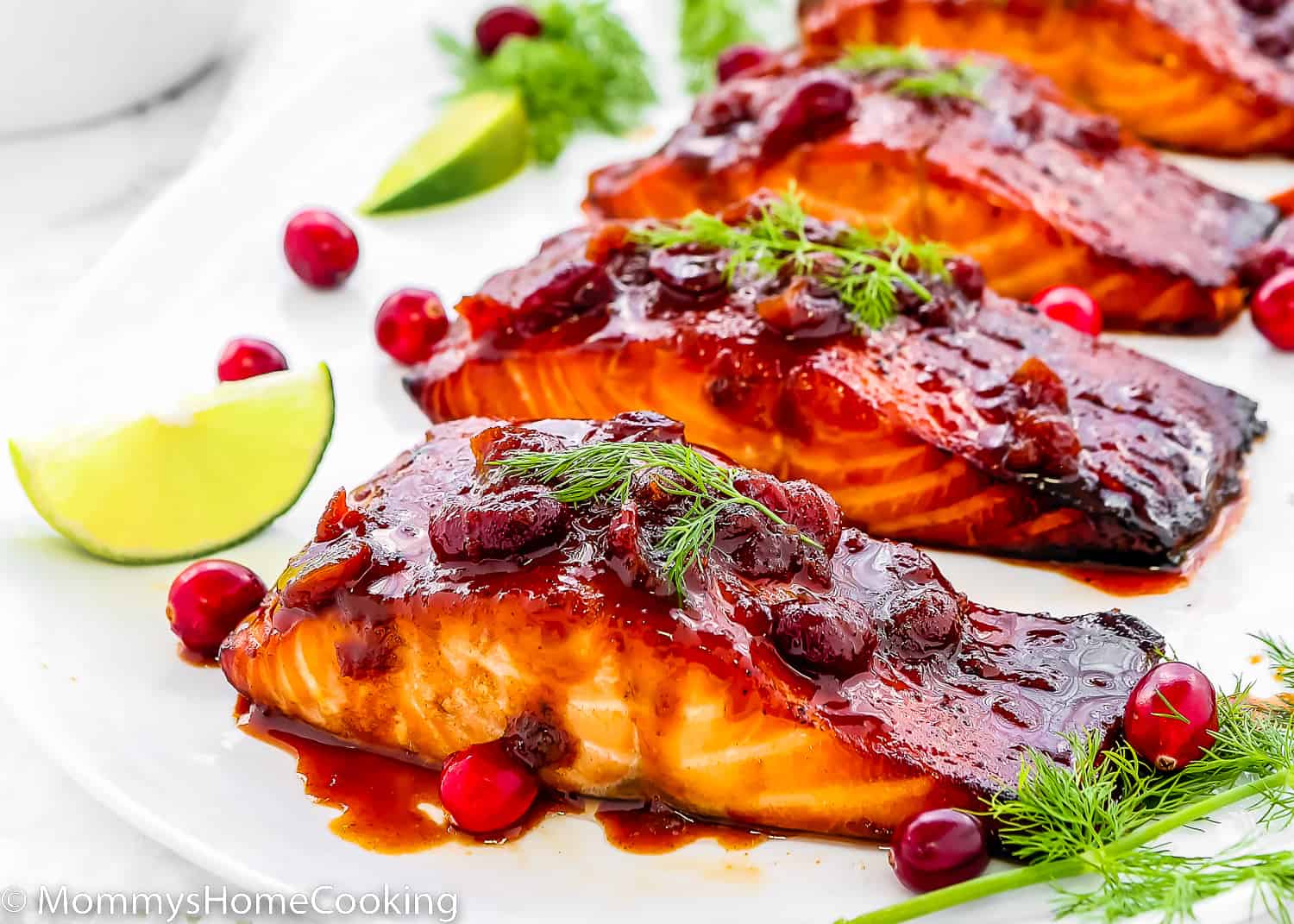 baked Cranberry Honey Glazed Salmon in a serving plate with fresh cranberries, lemon slices, dill and fresh cranberries.