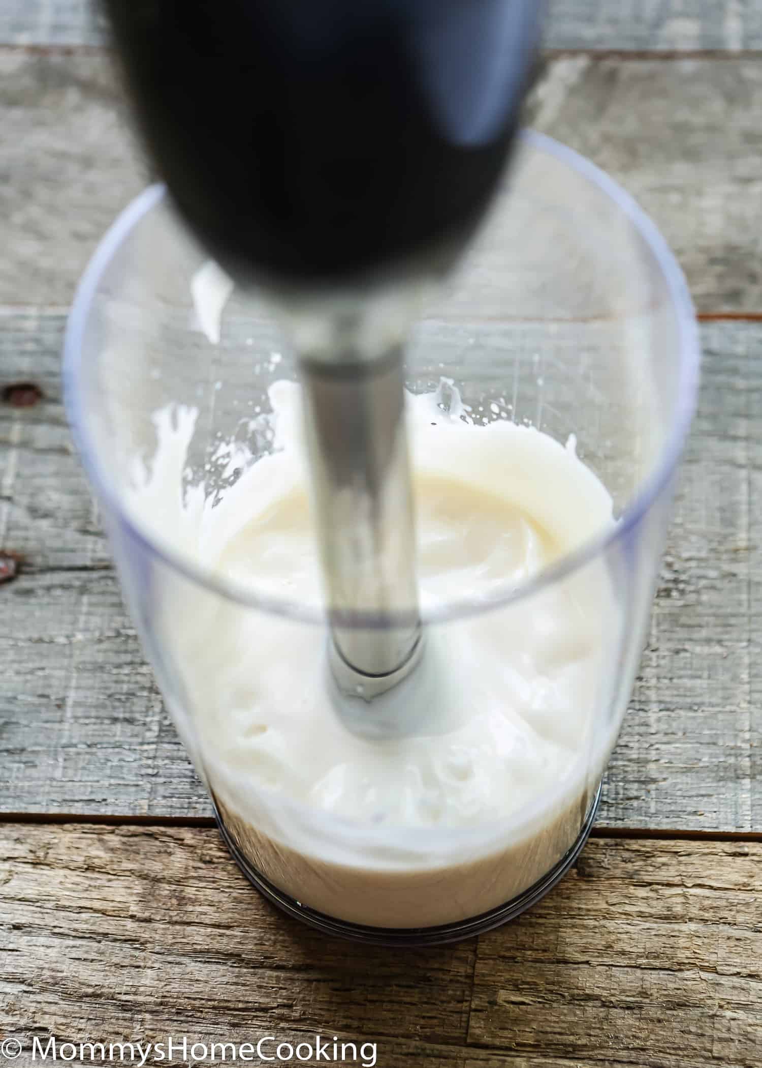 a immersion blender blending eggless mayonnaise in a cup.