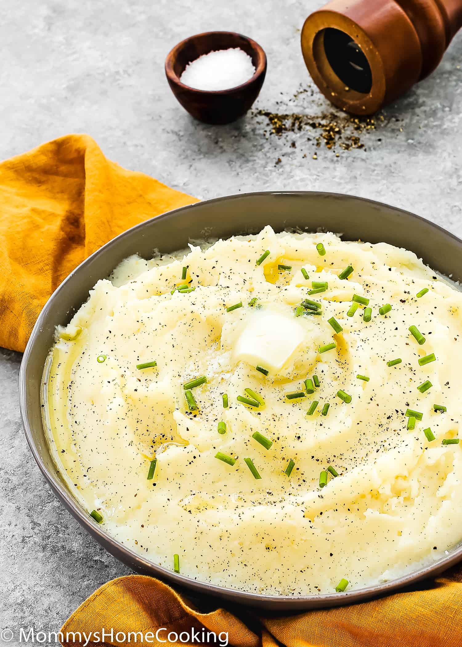 mashed potatoes in a serving bowl with butter and chives on over a gray surface.