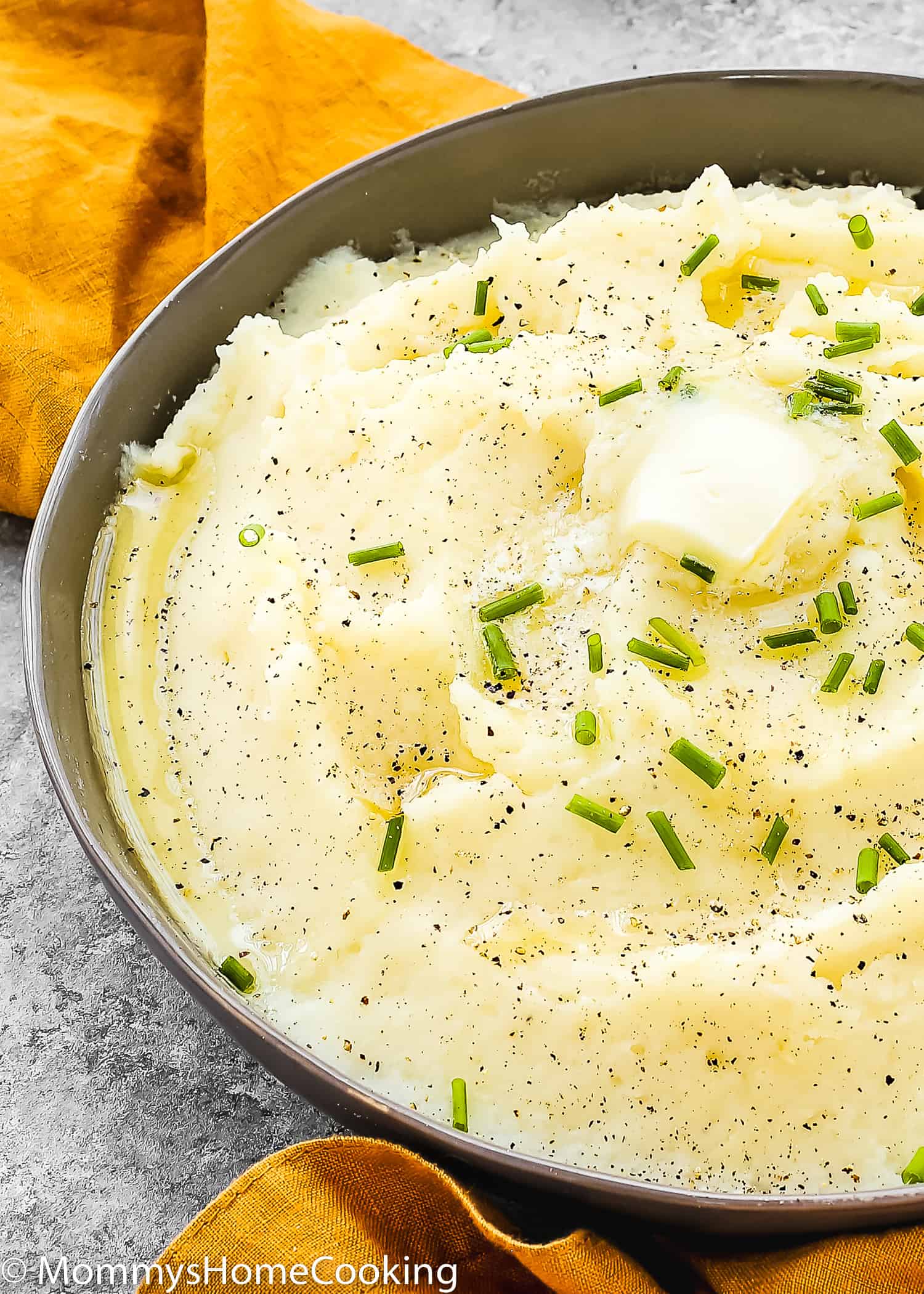 mashed potatoes in a serving bowl with butter and chives on top.