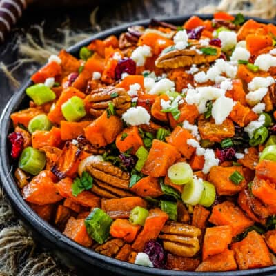 Roasted Sweet Potato and Cranberry Salad in a black serving bowl over a wooden surface and two serving spoons on the background.