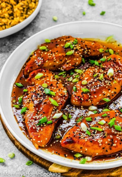 Asian-Style sticky Chicken Breasts in a white skillet garnished with green onion and sesame seeds.